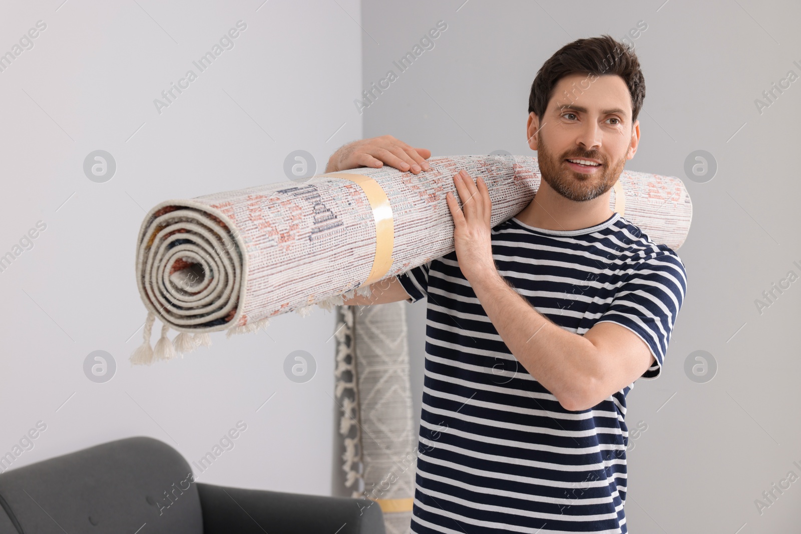 Photo of Smiling man holding rolled carpet in room