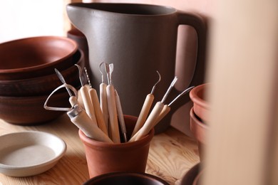 Set of different crafting tools and clay dishes on wooden table in workshop