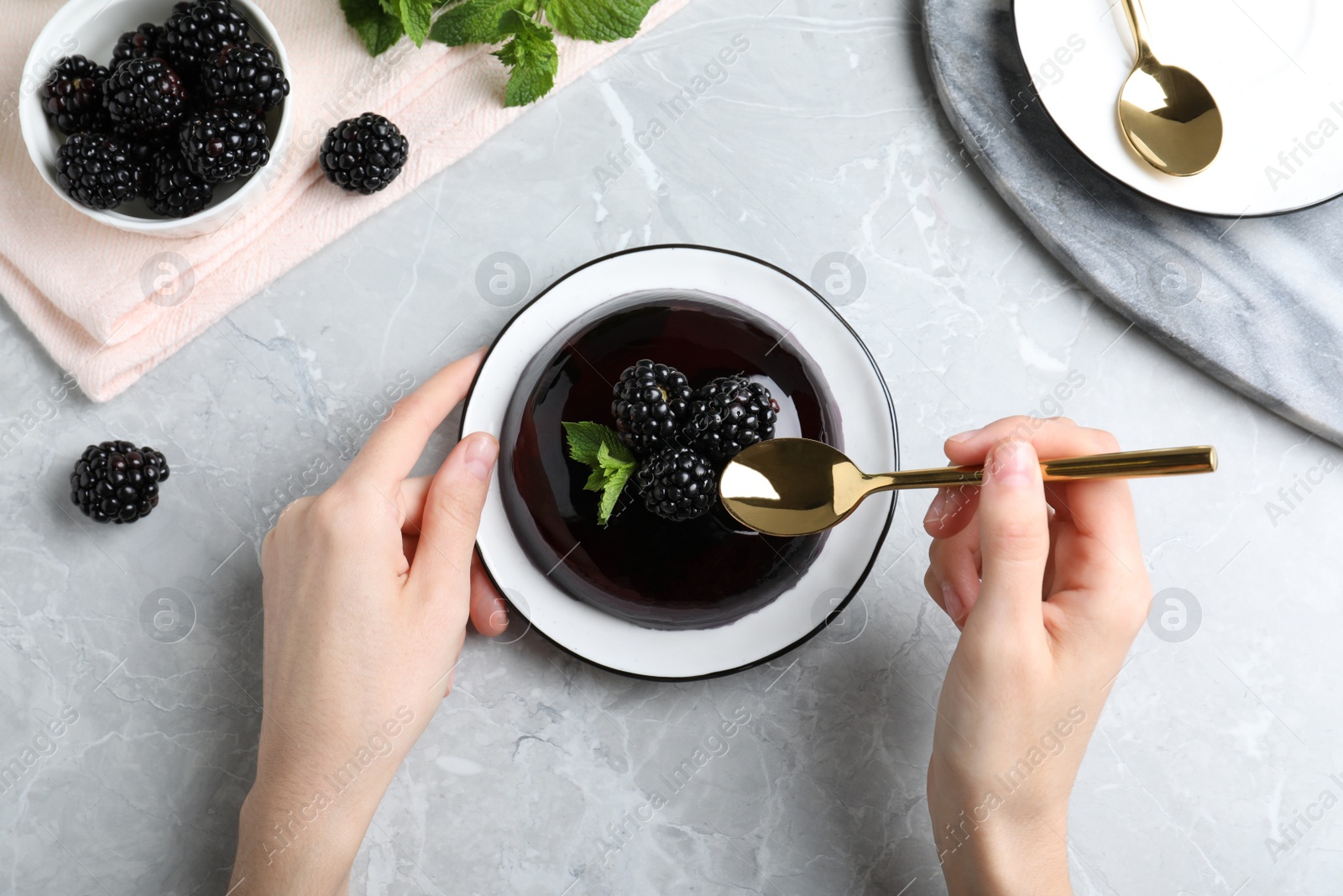 Photo of Woman eating delicious jelly with blackberries at grey table, top view