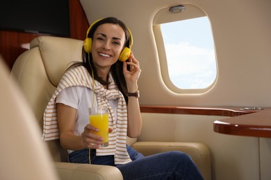 Photo of Young woman with glass of juice and headphones listening to music in airplane during flight