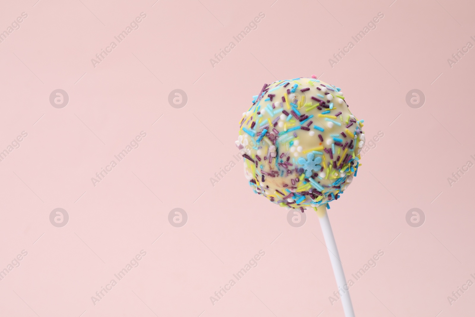 Photo of Delicious confectionery. Sweet cake pop decorated with sprinkles on pale pink background, closeup. Space for text