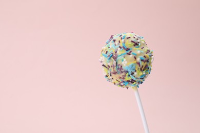 Photo of Delicious confectionery. Sweet cake pop decorated with sprinkles on pale pink background, closeup. Space for text
