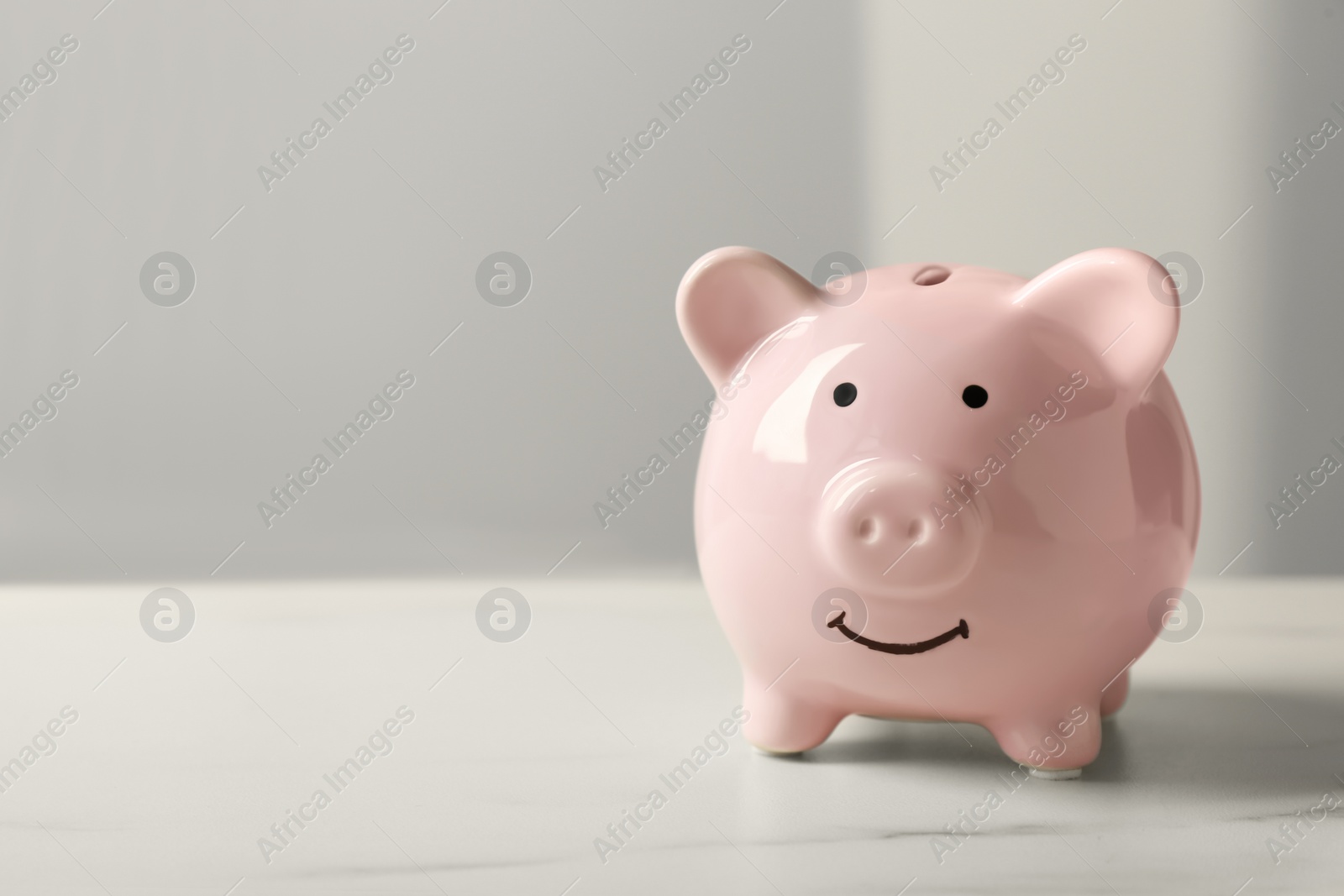 Photo of Ceramic piggy bank on white marble table. Space for text