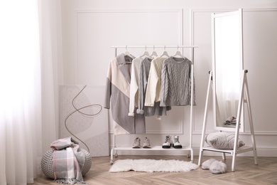 Rack with stylish warm clothes and mirror in dressing room
