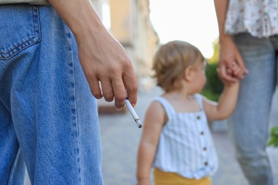 Photo of Woman smoking cigarette in public place outdoors, closeup. Don't smoke near kids
