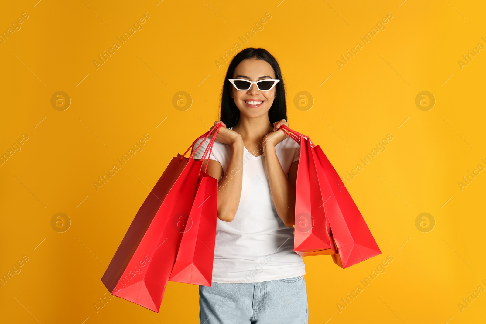 Photo of Beautiful young woman with paper shopping bags on yellow background