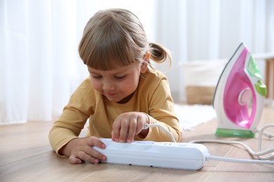 Photo of Little child playing with power strip and iron plug on floor indoors. Dangerous situation