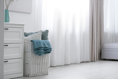 Photo of Basket with soft plaid and pillows in room. Space for text