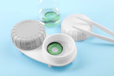 Photo of Case with green contact lenses and tweezers on light blue background, closeup