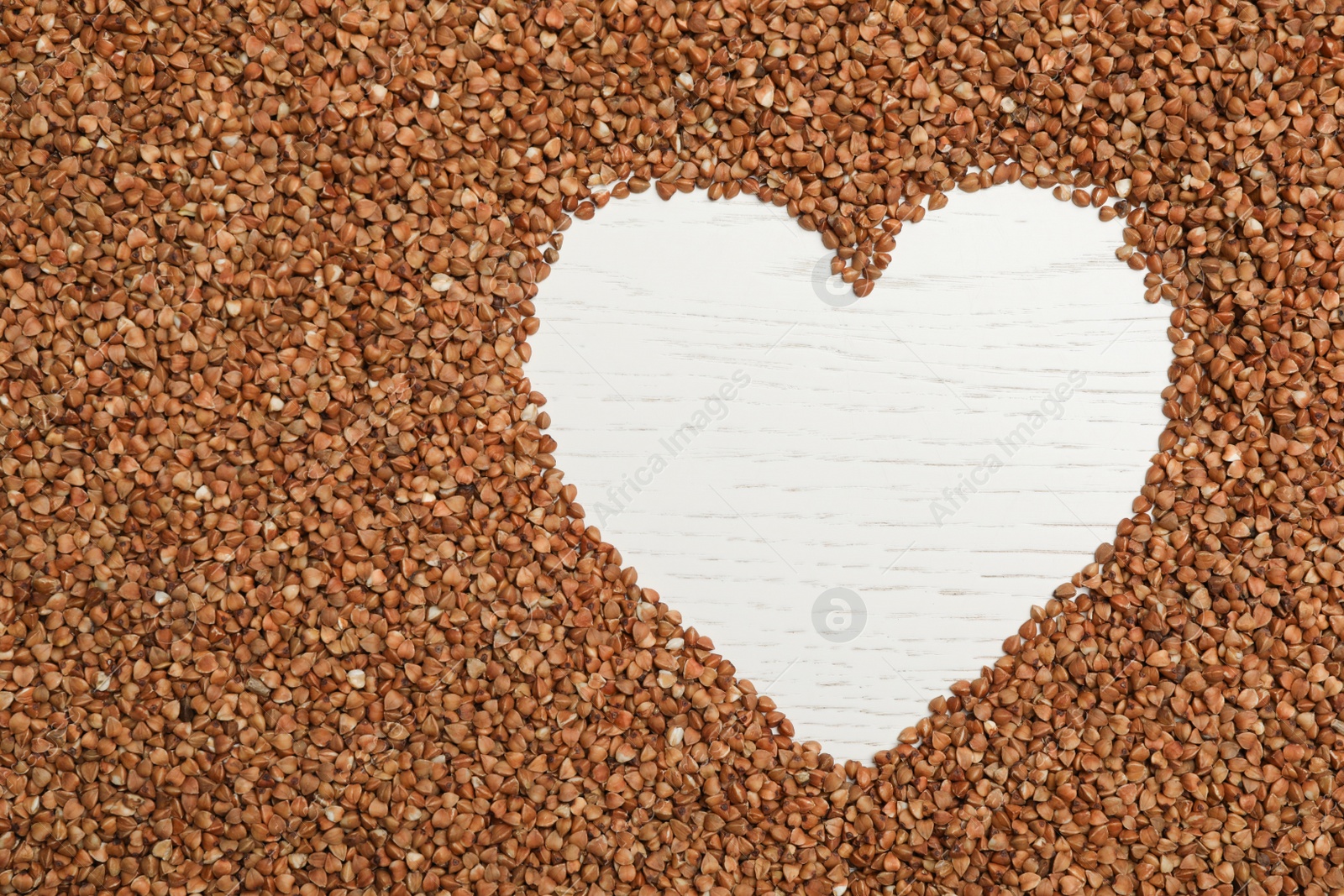 Photo of Heart shaped frame made of buckwheat grains on white wooden table, top view. Space for text