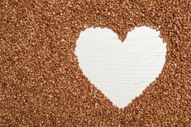 Photo of Heart shaped frame made of buckwheat grains on white wooden table, top view. Space for text