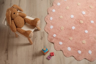Photo of Round pink rug with polka dot pattern and toys on wooden floor in baby's room, above view
