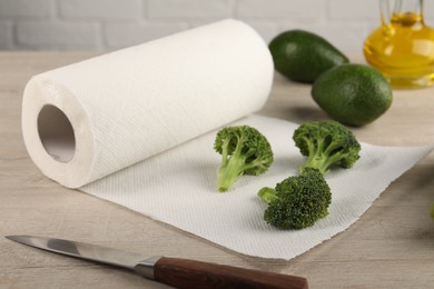 Photo of Paper towels, broccoli, avocados and knife on light wooden table, closeup