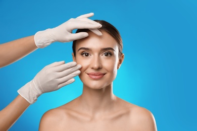 Photo of Doctor examining woman's face before plastic surgery on light blue background