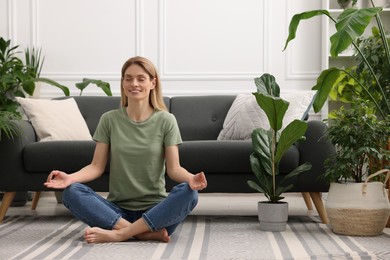 Photo of Woman meditating surrounded by beautiful potted houseplants at home