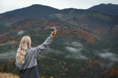 Photo of Young woman with modern drone in mountains, back view. Space for text