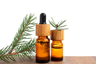 Bottles of pine essential oil and tree branch on wooden table against white background