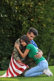 Photo of Man in military uniform with American flag hugging his wife at green park