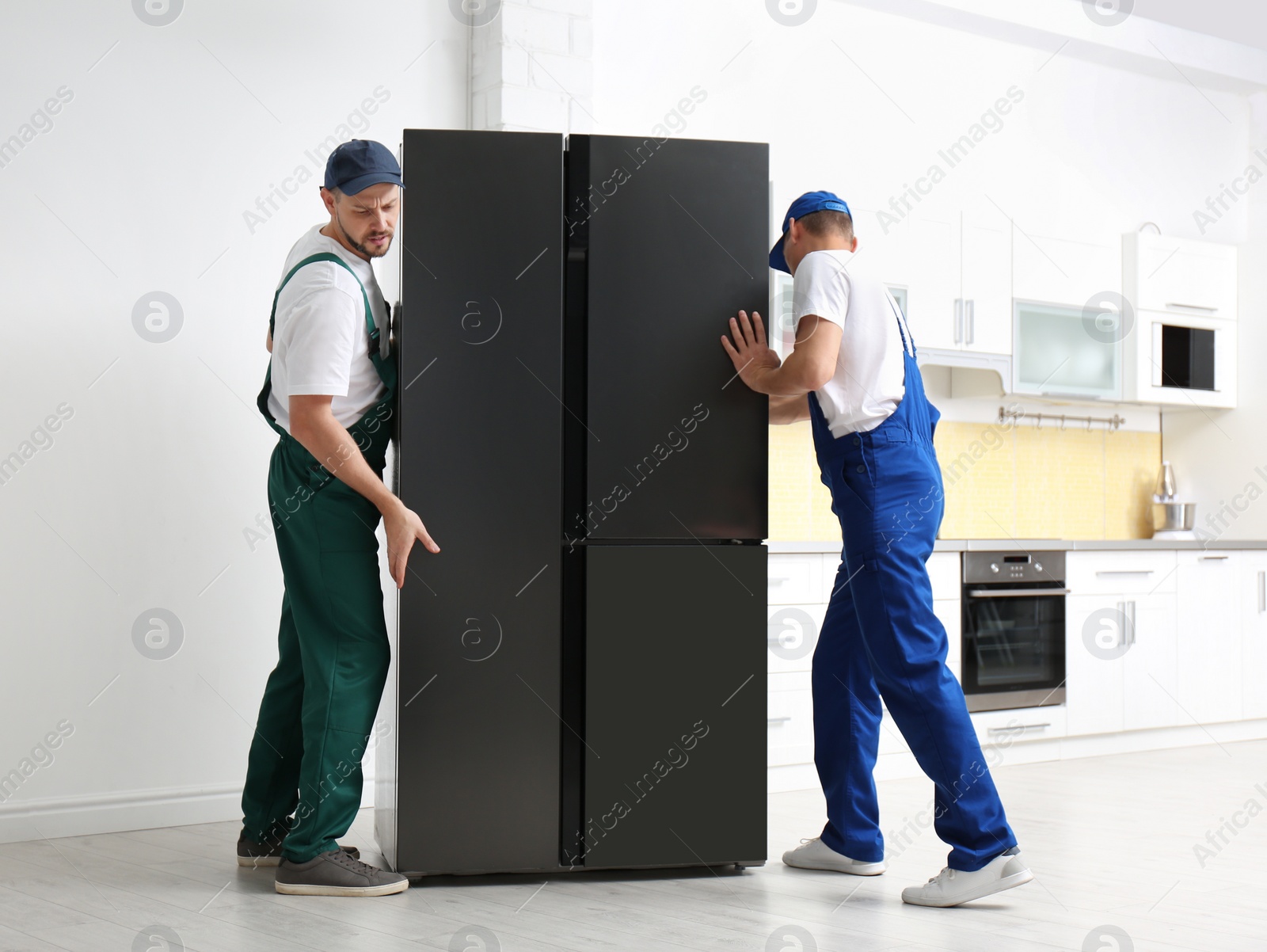 Photo of Professional workers carrying modern refrigerator in kitchen