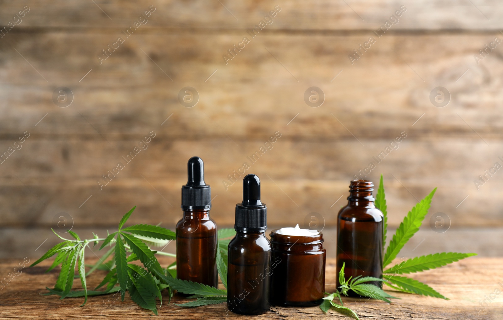 Photo of Cream, hemp leaves, bottles of CBD oil and THC tincture on wooden table