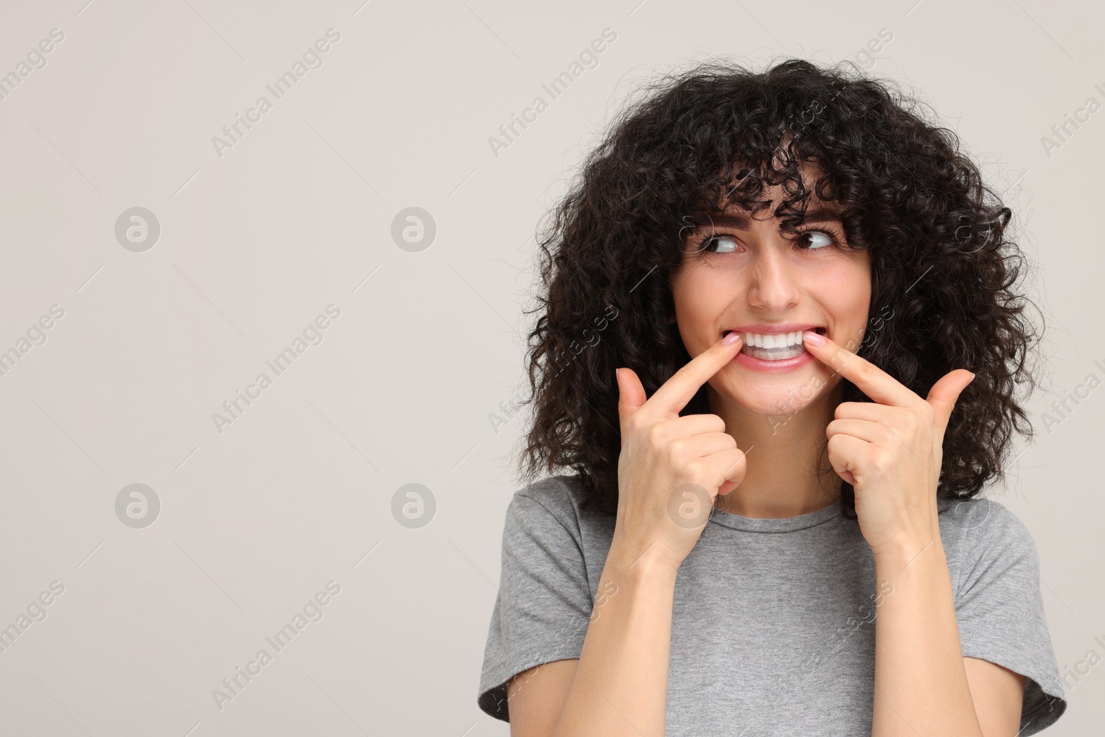 Photo of Young woman applying whitening strip on her teeth against light grey background, space for text