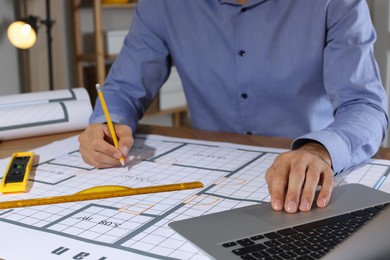 Photo of Architect working with construction drawings and laptop in office, closeup