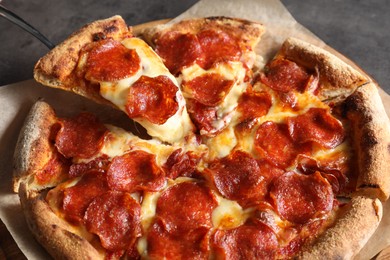 Taking piece of tasty pepperoni pizza at grey table, closeup