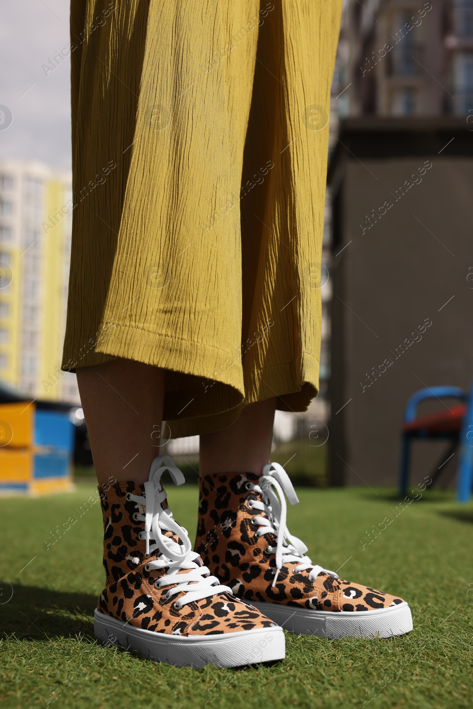 Photo of Woman wearing sneakers with leopard print on green grass outdoors, closeup