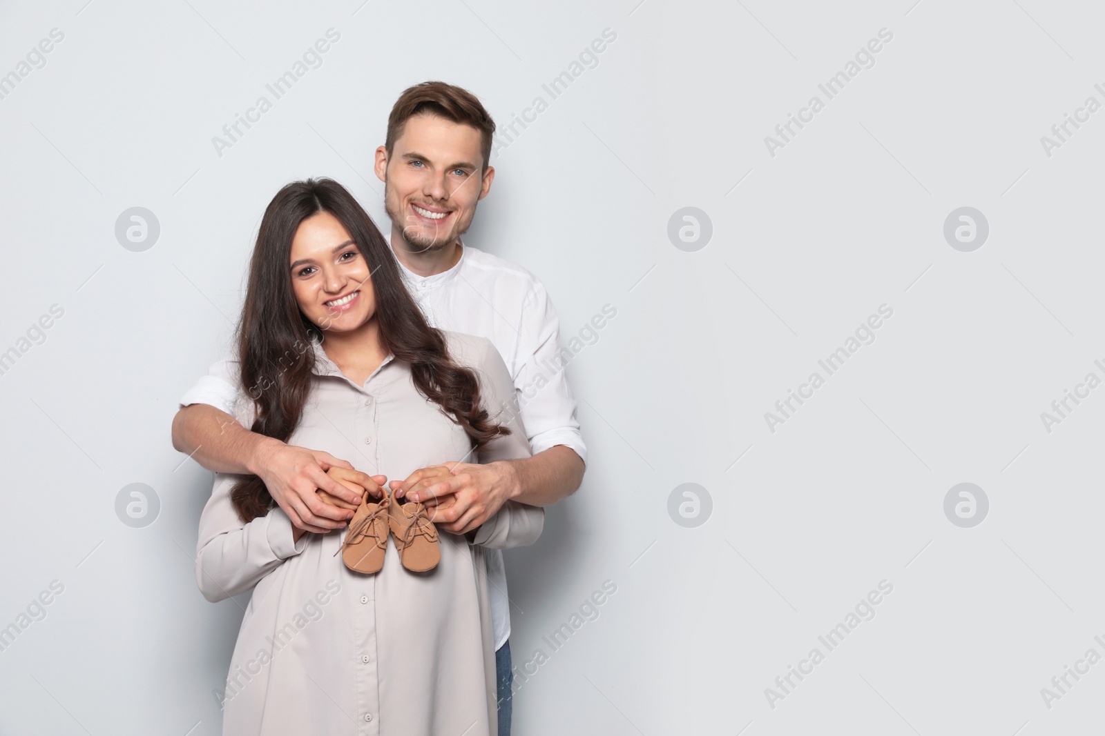 Photo of Pregnant woman and her husband holding little shoes on color background. Space for text