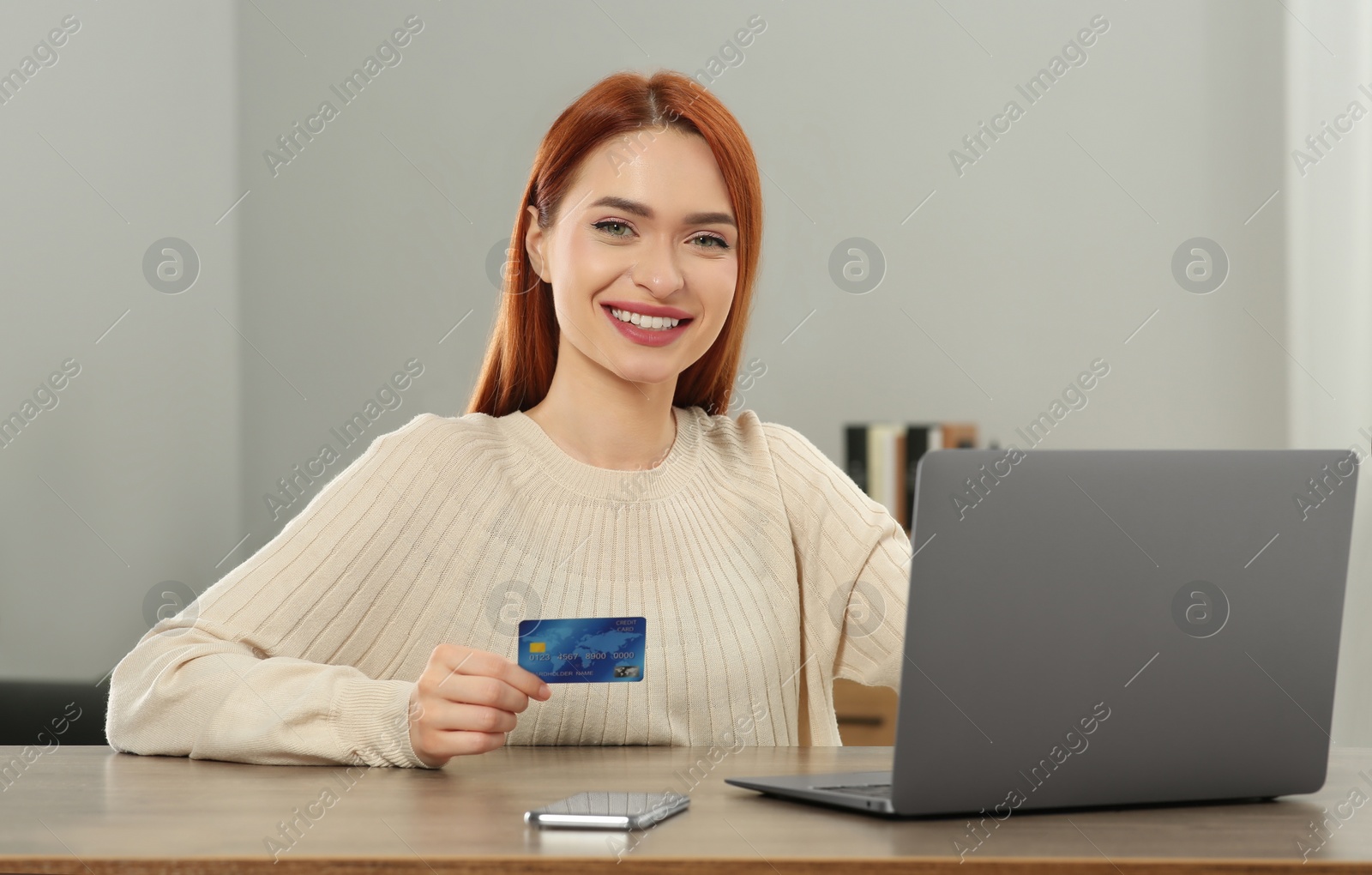 Photo of Happy woman with credit card using laptop for online shopping at wooden table in room