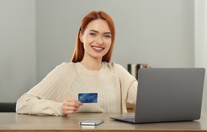 Photo of Happy woman with credit card using laptop for online shopping at wooden table in room