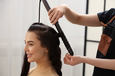 Hair styling. Hairdresser curling woman's hair in salon, closeup