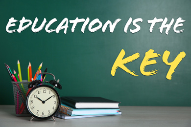 Alarm clock, school stationery and text EDUCATION IS THE KEY written on chalkboard in classroom. Adult learning