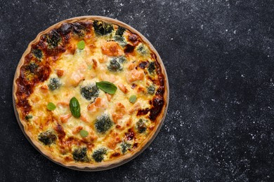 Photo of Delicious homemade quiche with salmon and broccoli on black table, top view. Space for text
