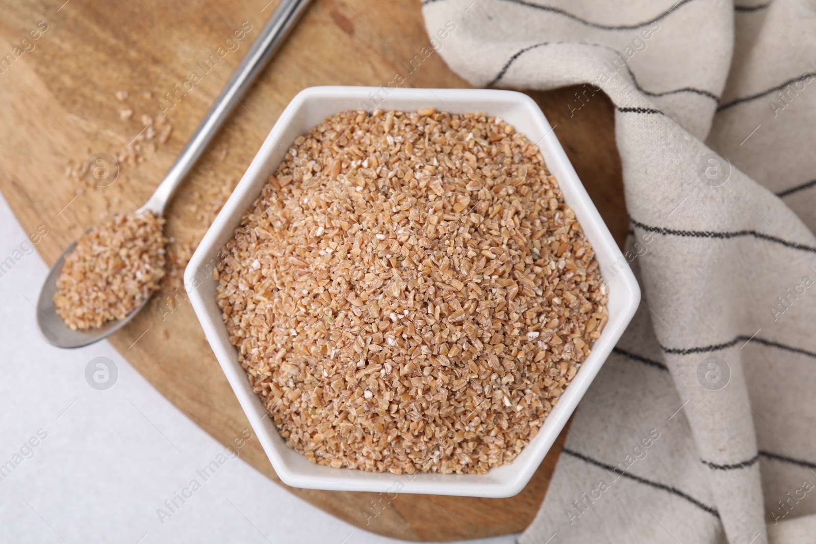 Photo of Dry wheat groats in bowl and spoon on light table, top view