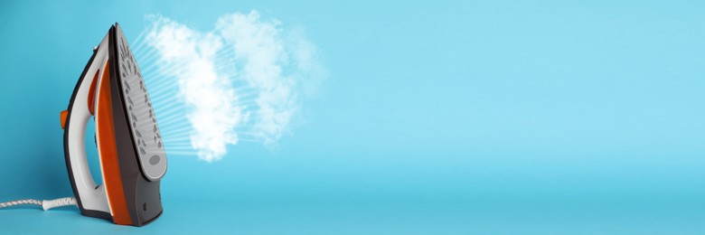 Image of Modern iron with steam on light blue background, space for text. Banner design