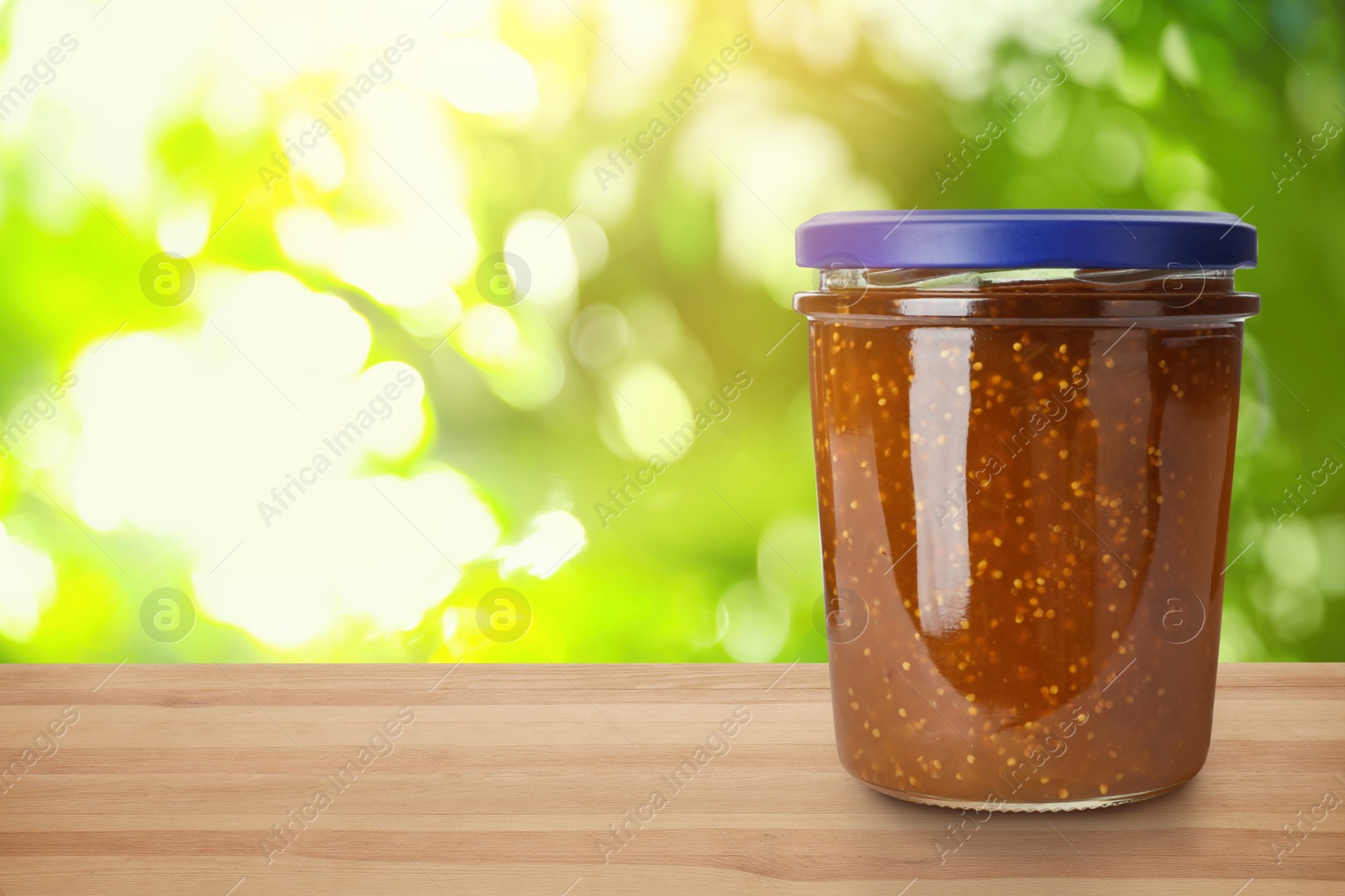 Image of Jar of fig jam on wooden table against blurred background, space for text