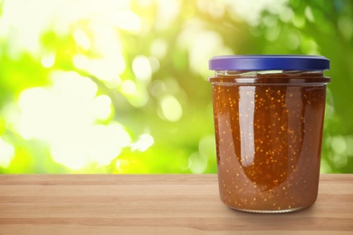 Image of Jar of fig jam on wooden table against blurred background, space for text