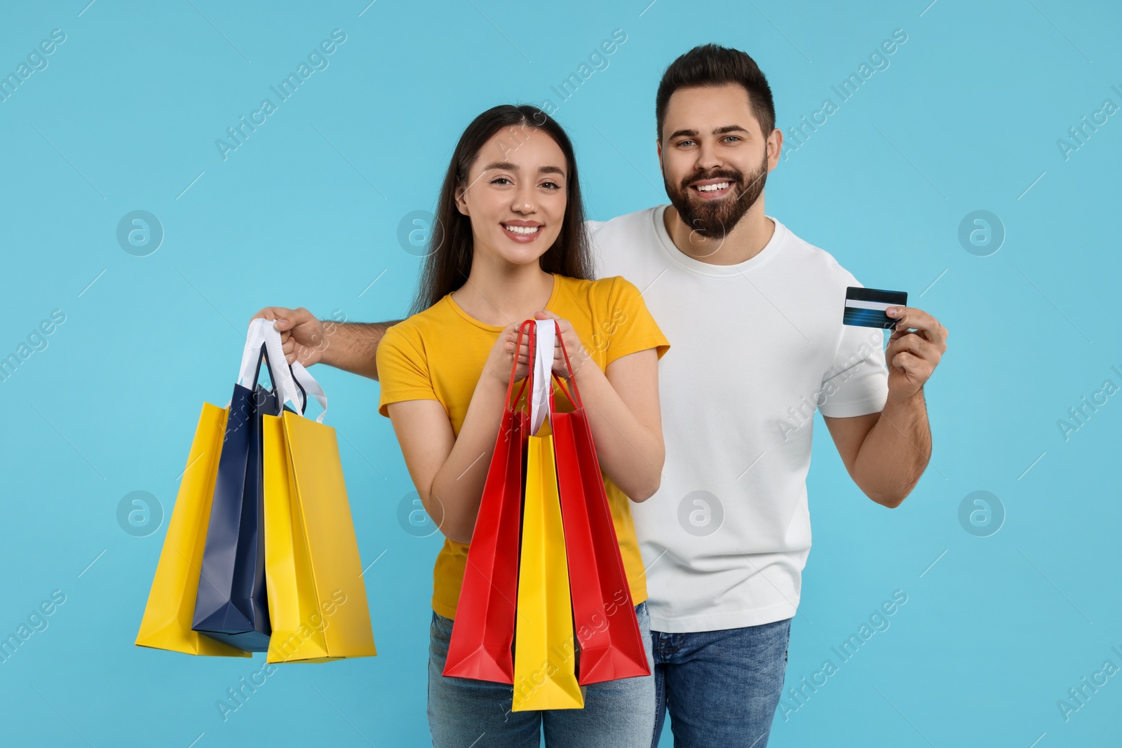 Photo of Happy couple with shopping bags and credit card on light blue background
