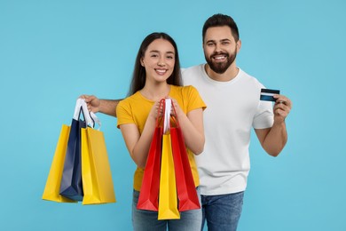 Happy couple with shopping bags and credit card on light blue background