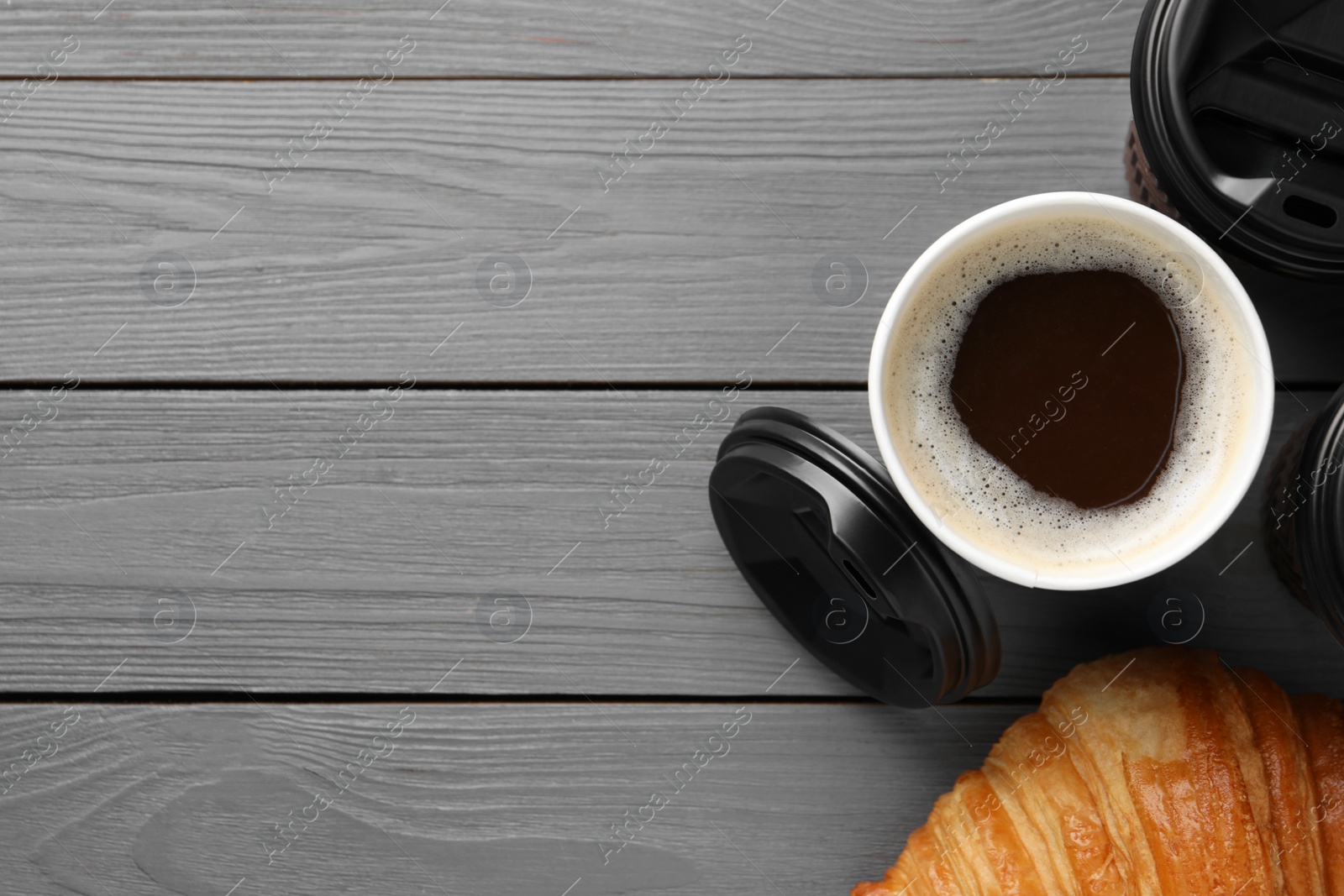 Photo of Coffee to go. Paper cups with tasty drink and croissant on grey wooden table, flat lay. Space for text