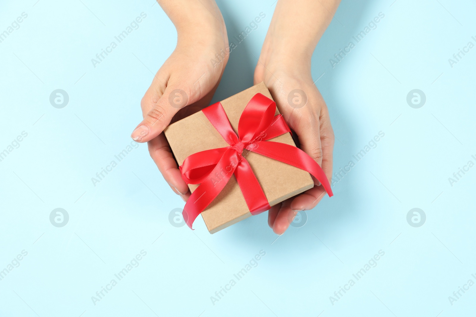 Photo of Woman holding gift box on light blue background, top view