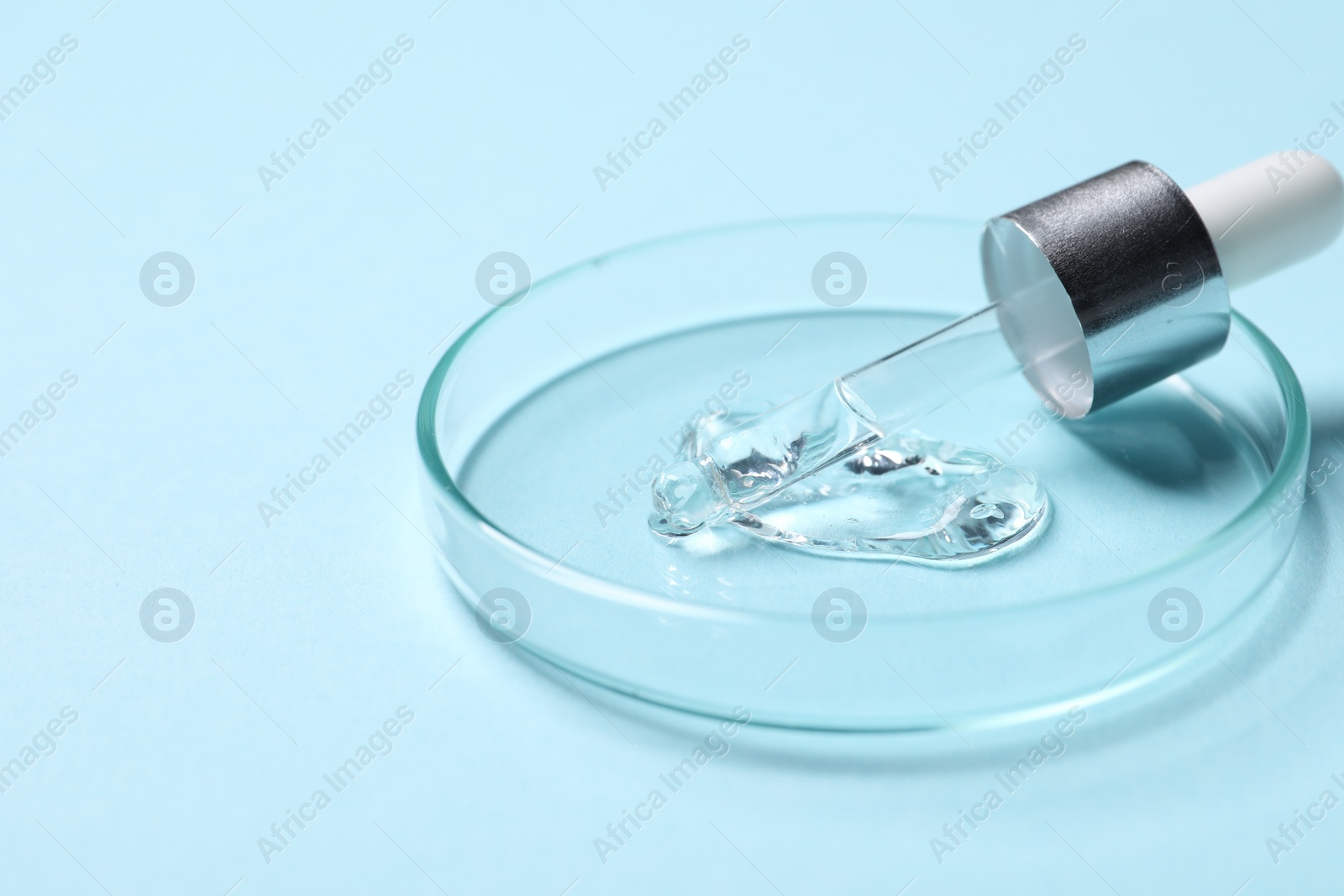Photo of Petri dish with sample of cosmetic serum and pipette on light blue background, closeup. Space for text