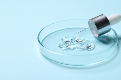 Photo of Petri dish with sample of cosmetic serum and pipette on light blue background, closeup. Space for text