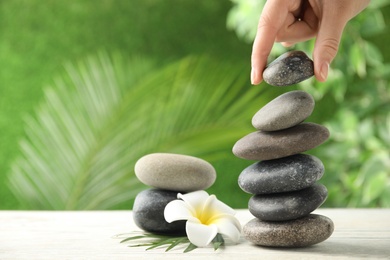 Photo of Woman stacking stones on table against blurred background, closeup. Zen concept