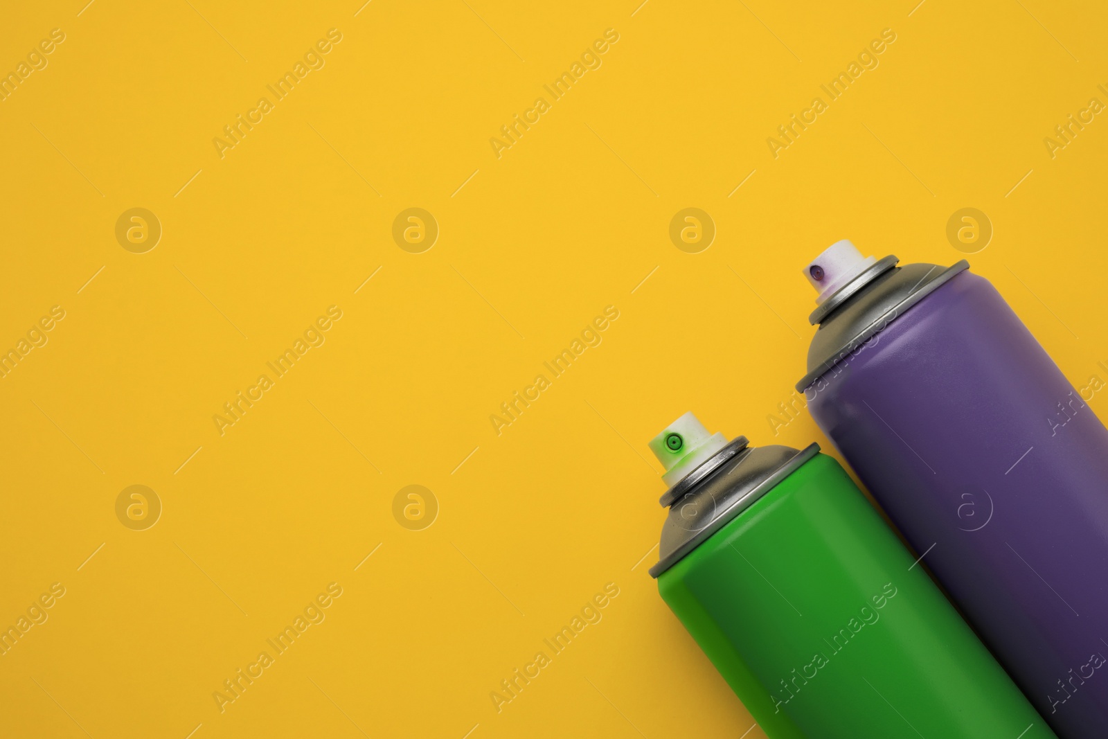 Photo of Cans of different graffiti spray paints on yellow background, flat lay. Space for text