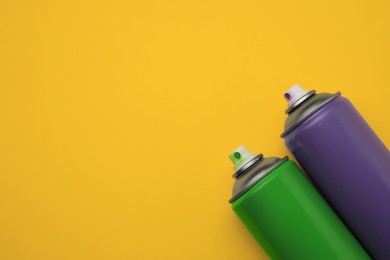 Photo of Cans of different graffiti spray paints on yellow background, flat lay. Space for text