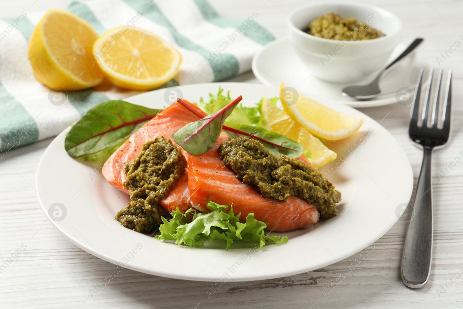 Photo of Tasty cooked salmon with pesto sauce served on white wooden table