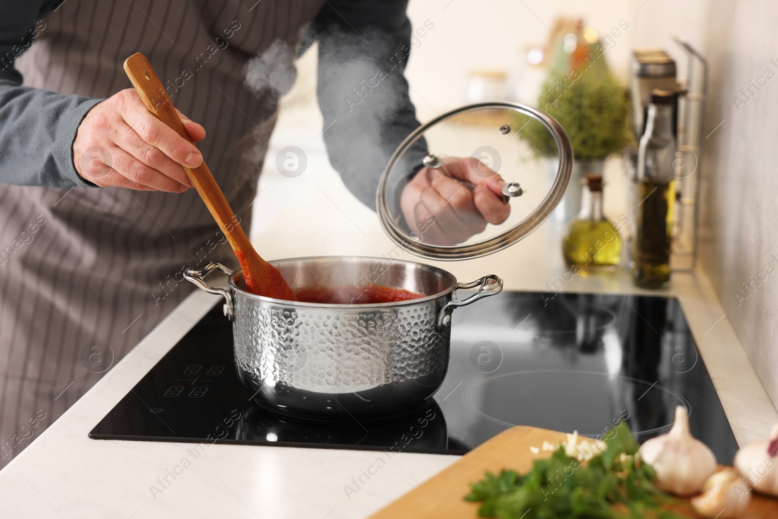 Photo of Man cooking tomato soup on cooktop in kitchen, closeup