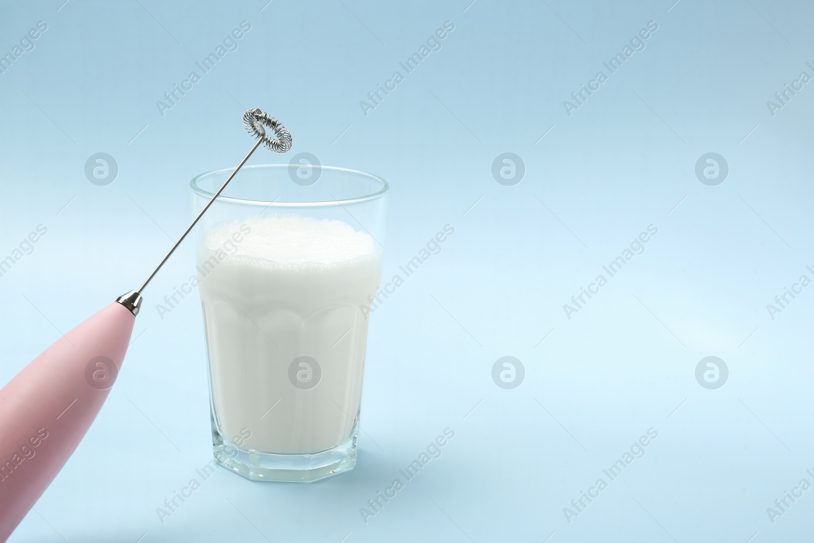 Photo of Mini mixer (milk frother) and whipped milk in glass on light blue background. Space for text